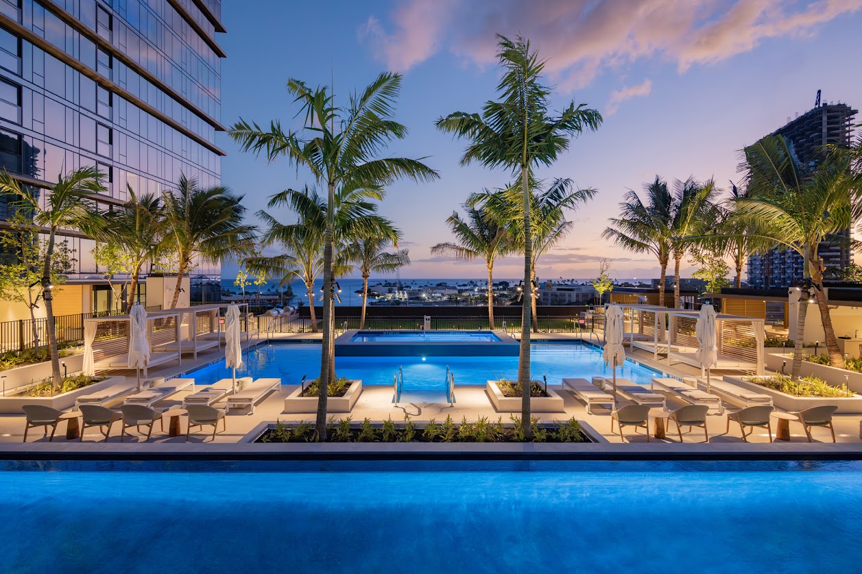 A pool surrounded by palm trees and lounge chairs.